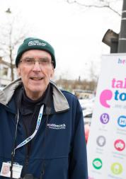 Man wearing a winter hat and stood in front of a Healthwatch banner